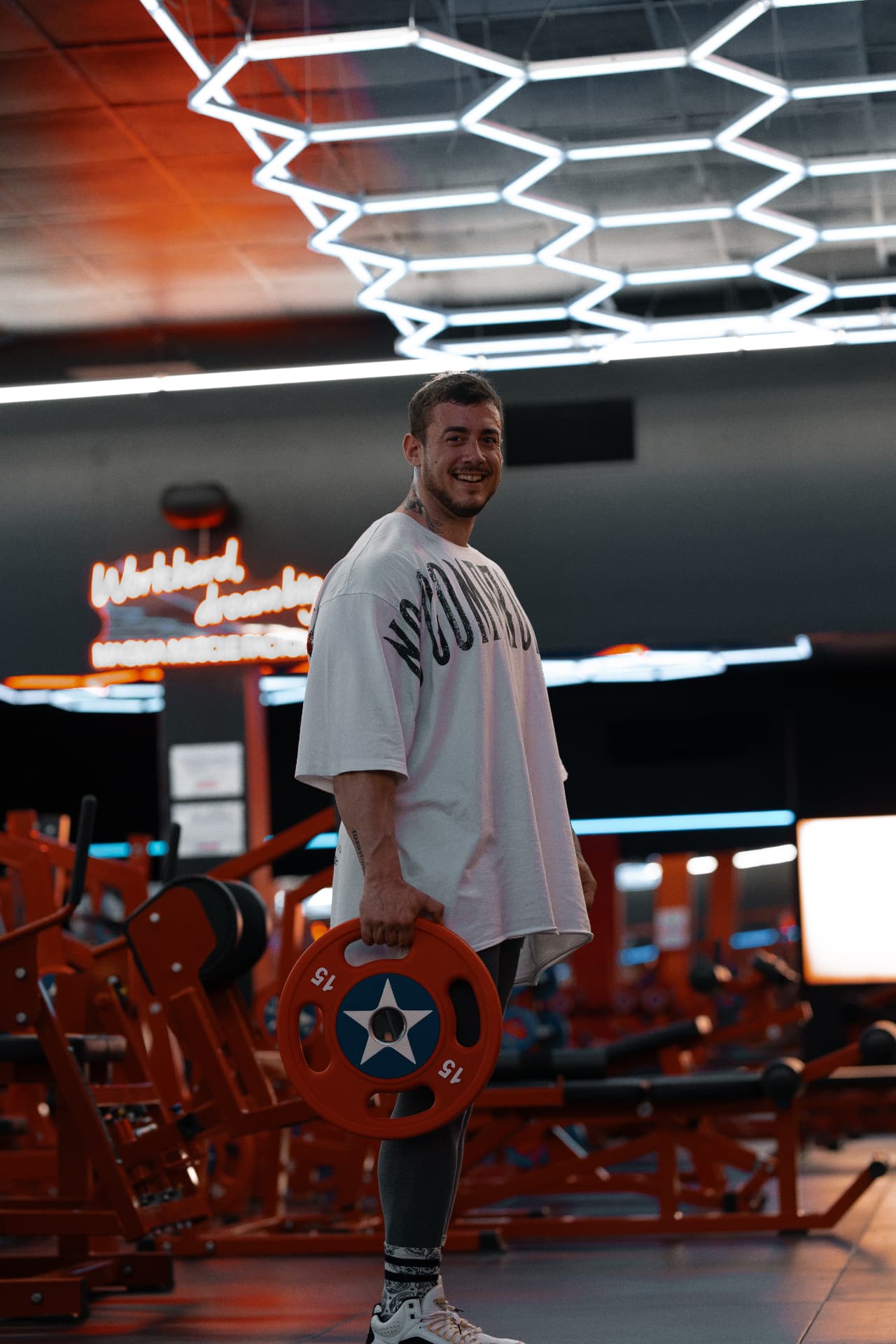 Sonriendo con un disco de 15 kg bajo las luces del gimnasio